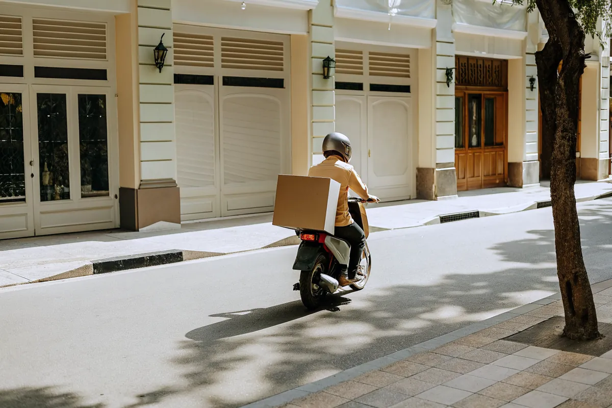 A delivery rider carrying a cardboard parcel along a quiet city street